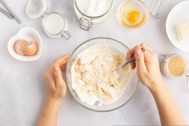 istock Various baking ingredients - flour, eggs, sugar, butter and kitchen utensils on grey background. Woman hands 1470205806
