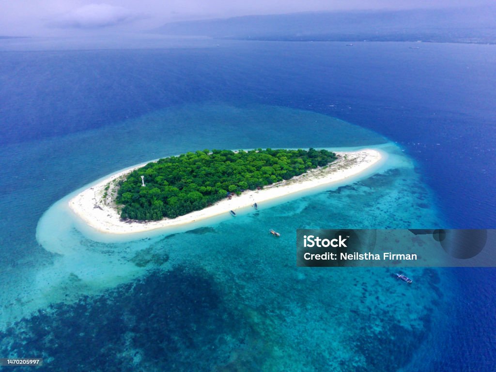 The Tabuhan Island in the beautiful clear waters of the Bali Straits. The small island named Tabuhan in the beautiful clear waters of the Bali Straits. Banyuwangi. Indonesia. Aerial footage taken with Drone. Bali Stock Photo