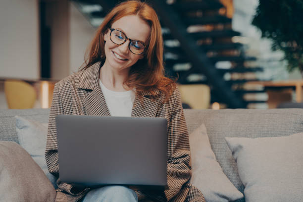 istock Happy female office worker chatting on laptop while sitting on grey couch at office 1470207181