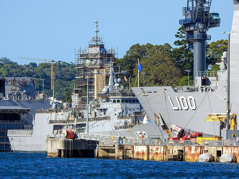 HMAS Warramunga (centre) is an Anzac Class frigate of the Royal Australian Navy and undergoing a refurbishment while docked at Garden Island Naval Base in Sydney Harbour.  On her left is the stern of the Amphibious Assault Ship, HMAS Adelaide.  On her right is the bow of HMAS Choules, which according to Navy's website, 