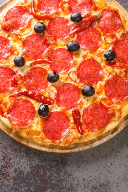 pizza diavola toppings mit peperoniwurst, käse, tomatensauce, chilischoten und schwarzen oliven hautnah auf einem holzbrett. vertikale draufsicht - devil chili stock-fotos und bilder