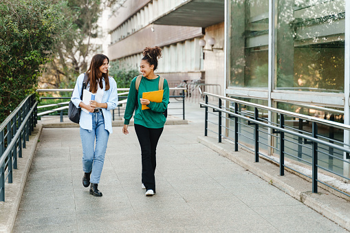 Two happy students walking and talking each other in University campus after classes