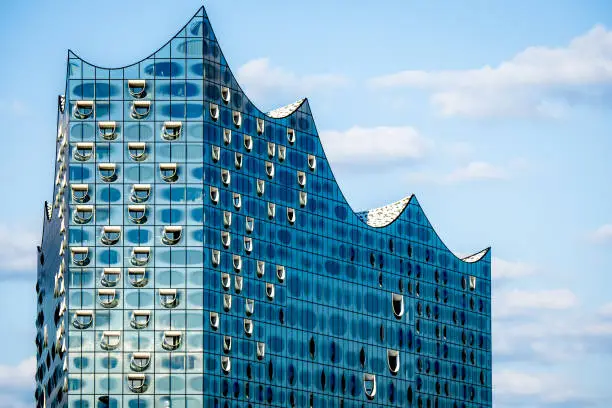 Stunning closeup of the famous glossy glass facade of the iconic Elbphilharmonie concert hall landmark in Hamburg, showcasing its modern, wave-like design and reflecting the sky above in sunlight.