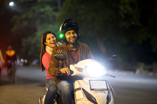 Young couple having fun riding on motor scooter at night