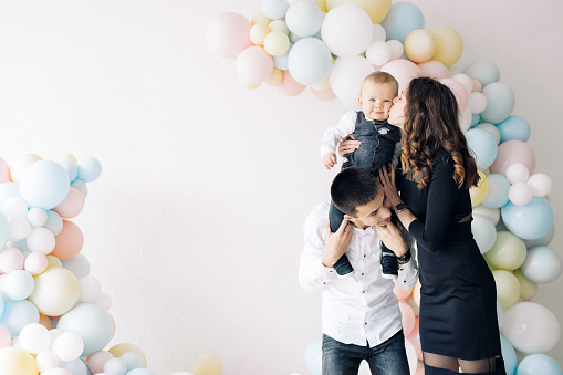 Happy family celebrates first birthday of baby boy among a lot of colorful balloons. Celebration first birthday. Festive event. Image with copy space.