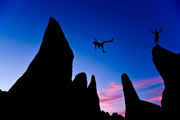 istock Two men climbing a rope between mountain peaks at dawn 147021508
