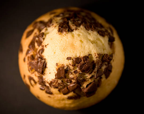 Young males taking chocolate muffin with almond slices. Close up of young men human hand holding a muffin.There is Chocolate muffin with raisin and almond slice on top. The muffin has a brown cover paper. There's collection of bread on the blurred backgrounds.