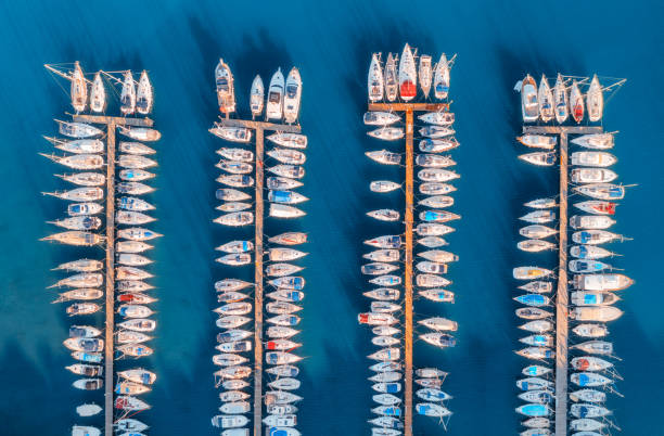 Aerial view of boats and luxure yachts in dock at sunset in summer in Pula, Croatia. Colorful landscape with sailboats and motorboats in sea bay, jatty, clear blue sea. Drone view of harbor. Travel stock photo
