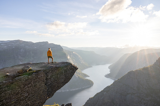 Female hiker standing on Trolltunga (troll tongue) famous rock high above a lake with panoramic view of the valley, popular tourist adventure trek in Norway