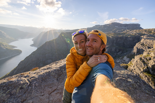 They smile at the camera, showing the magnificent view of the fjord and mountains