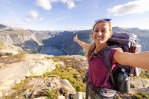 She smiles at the camera, showing the magnificent view of the fjord and mountains