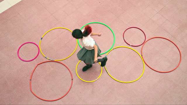 Agile schoolgirl hopscotching through plastic hoops