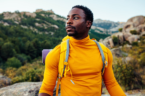 Hiker young adult african american man with backpack and trekking sticks at the foot of the mountain