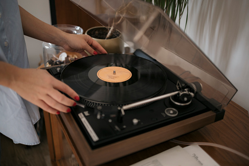 Close-up of a woman playing vinyl record on turntable. Cropped shot of a female hands placing vinyl music disc on gramophone at home.