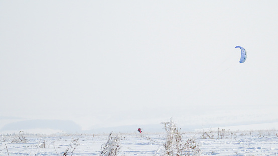 A girl in a red jumpsuit is kiting on skis in snowy winter terrain.