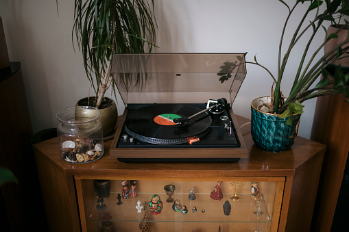 Turntable playing vinyl LP record at home. Old gramophone with old vinyl music record on side cabinet in living room.