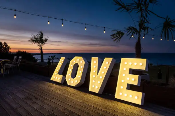 wedding hall interiors and decorations illuminated love inscription against the background of the evening sky with palm trees, a sea bay in the background during the blue hour