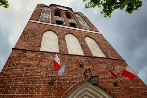 brick church tower against a cloudy sky, bottom view with flags of poland and vatican