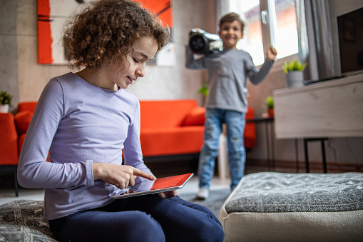 A brother and sister are staying in the living room and using a digital tablet, surfing the Internet and watching educational shows for children