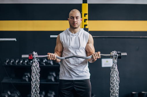 One man, fit male exercising with barbell and chains in gym.