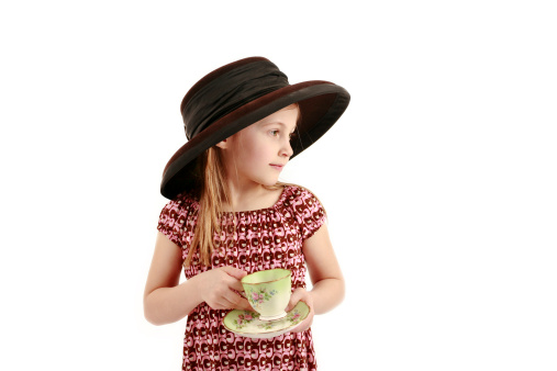 A side shot of a young girl dressed up in a hat holding a cup of tea with a saucer set on an isloated white background with copy space.