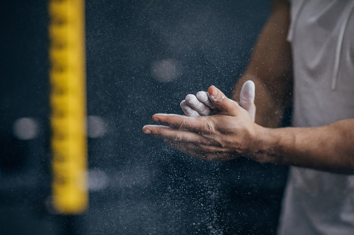 One man, unrecognizable male applying talcum powder on hands in gym.