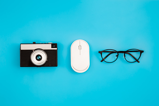 Vintage camera, glasses and computer mouse on a blue background isolated, flat lay.