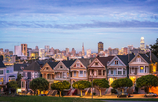 The row of traditional Victorian style townhouses in San Francisco, known as the Painted Ladies, photographed in the blue hour after sunset, with the lights of the city on the horizon.