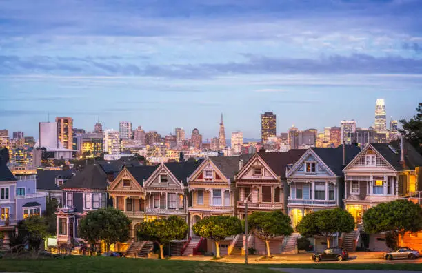 The row of traditional Victorian style townhouses in San Francisco, known as the Painted Ladies, photographed in the blue hour after sunset, with the lights of the city on the horizon.