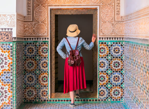 Colorful traveling by Morocco. Young woman in red dress walking in Ben Youssef Madrasa, Marrakech Morocco stock photo