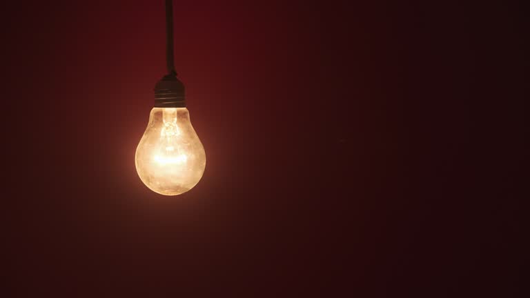 Incandescent Lamp Glows and Flickers on Dark Red Background, Place for Text