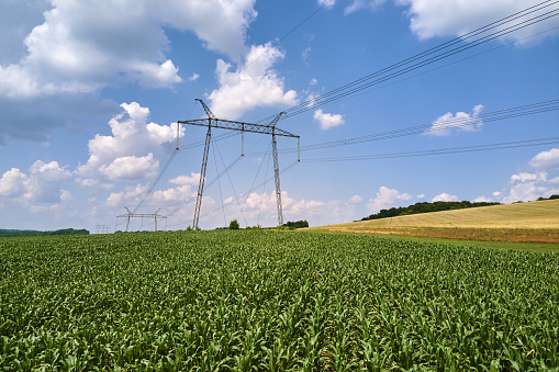 High voltage tower with electric power lines between green agricultural fields. Transfer of electricity concept.