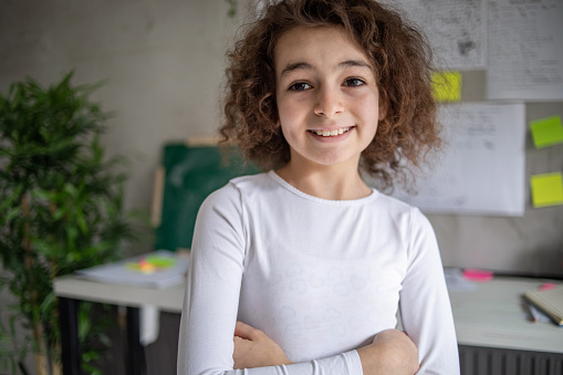 Portrait of a happy Caucasian girl in the children's room, she stands and stares at the camera, the working part of her children's room can be seen from her