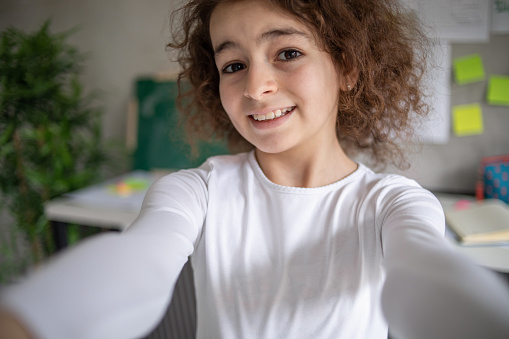 A teenage girl is recording her blog, looking at the mobile phone camera and talking directly to her live followers, she is in her children's room