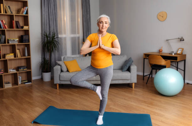 istock Yoga practice on retirement. Calm senior lady standing in tree pose, keeping balanced, exercising on yoga mat at home 1470239886