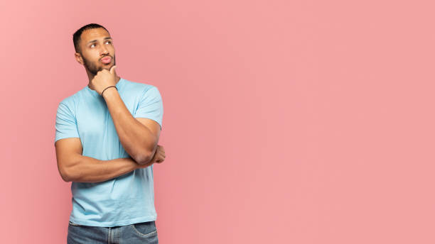 istock Pensive african american man thinking and touching chin, looking aside at copy space, posing over pink background 1470239913