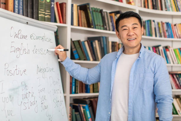 istock Joyful Asian Teacher Man Near Whiteboard Standing In Classroom 1470240000