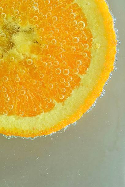 Close-up of fresh orange slice on white background. Slice of orange in sparkling water on white background, close-up. Horizontal image.ice in liquid with bubbles. Slice of orange fruit in water. Close-up of fresh orange fruit slice covered by bubbles. Ver stock photo