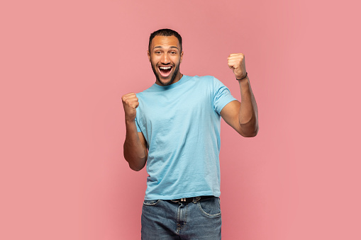 Overjoyed young black man screaming in excitement, gesturing YES with both hands on pink studio background. Triumphant millennial African American guy shouting WOW, celebrating success