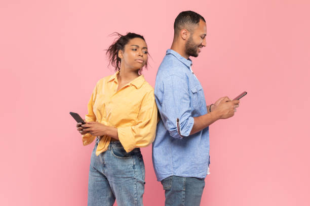 istock Curious black lady trying to look at her boyfriend's smartphone, guy using gadget and chatting, standing back to back 1470240106