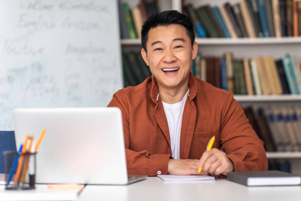 istock Japanese Teacher Man Sitting At Laptop Taking Notes In Classroom 1470240127