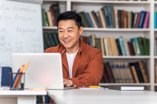 istock Cheerful Asian Tutor Man Using Laptop Teaching Online At Workplace 1470240130