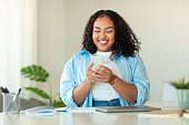 Happy Black Woman Using Mobile Phone Sitting In Modern Office