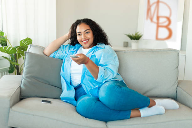 istock Black Woman Turning On TV With Remote Controller At Home 1470240702
