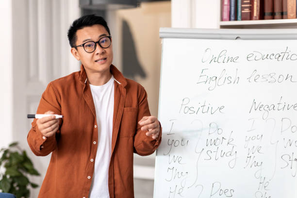 istock Japanese Male Teacher Talking Looking At Camera Standing In Classroom 1470240813