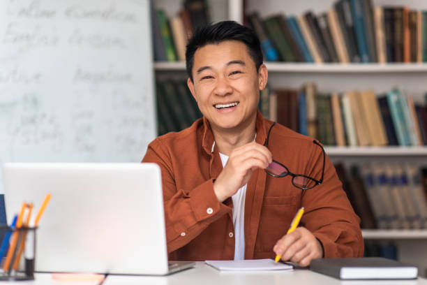 istock Cheerful Korean Teacher Man Near Laptop Taking Notes At Workplace 1470240833