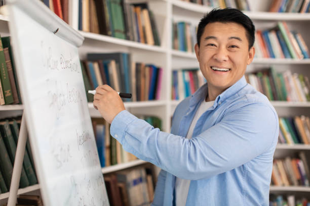 istock Cheerful Japanese Tutor Man Writing On Whiteboard Having Lesson Indoor 1470240834