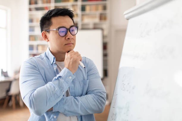 Thoughtful Asian Man Teacher Thinking Looking At Whiteboard In Classroom