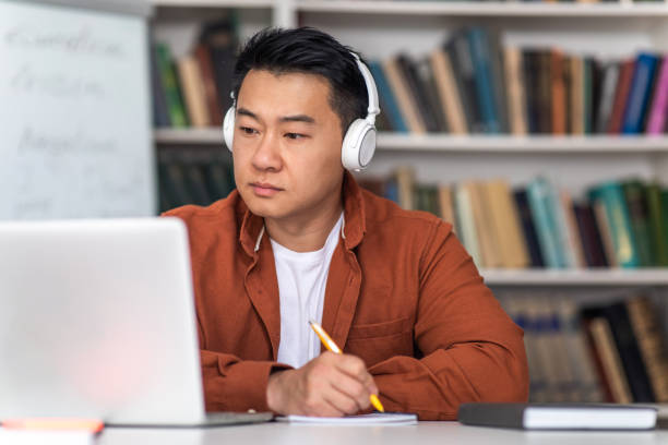 istock Chinese Teacher Man Using Laptop Taking Notes Sitting In Classroom 1470240836