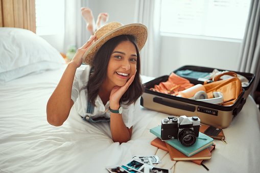 Travel, luggage and woman on bed with clothes, camera and suitcase for adventure, holiday and vacation. Traveling lifestyle, freedom and portrait of girl in bedroom pack for journey, tourism and trip